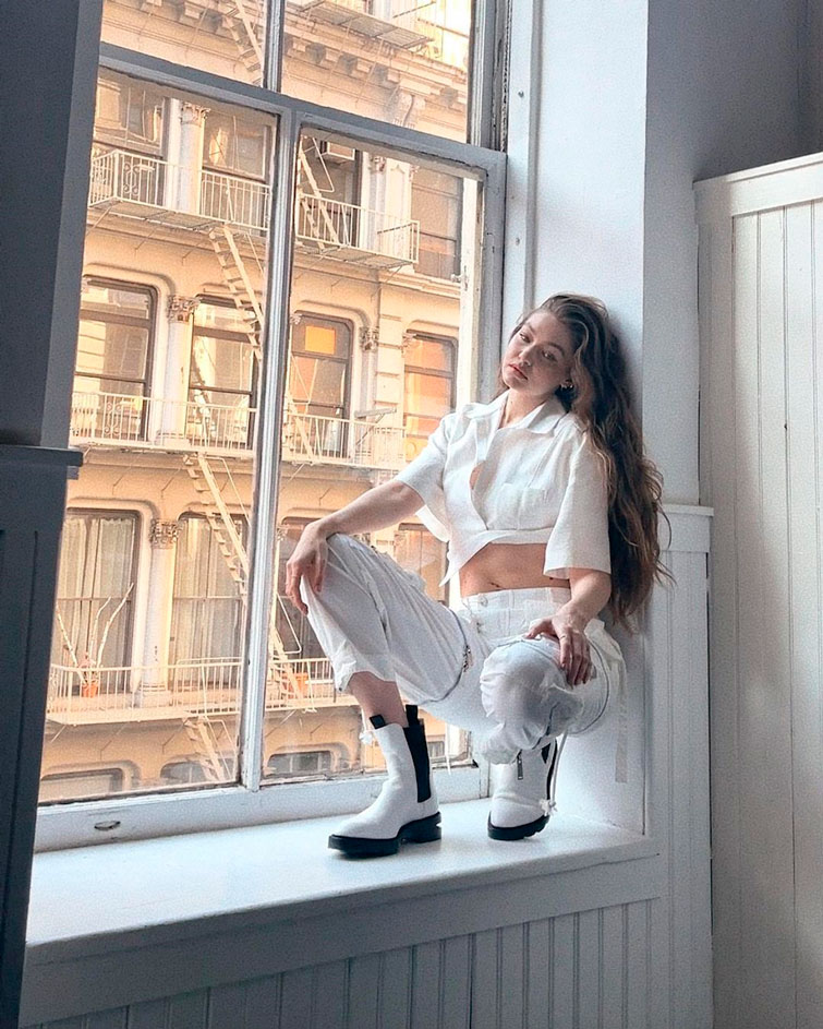 Gigi Hadid, modelo com outfit com camisa branca cropped acompanhado de umas calças e botas brancas